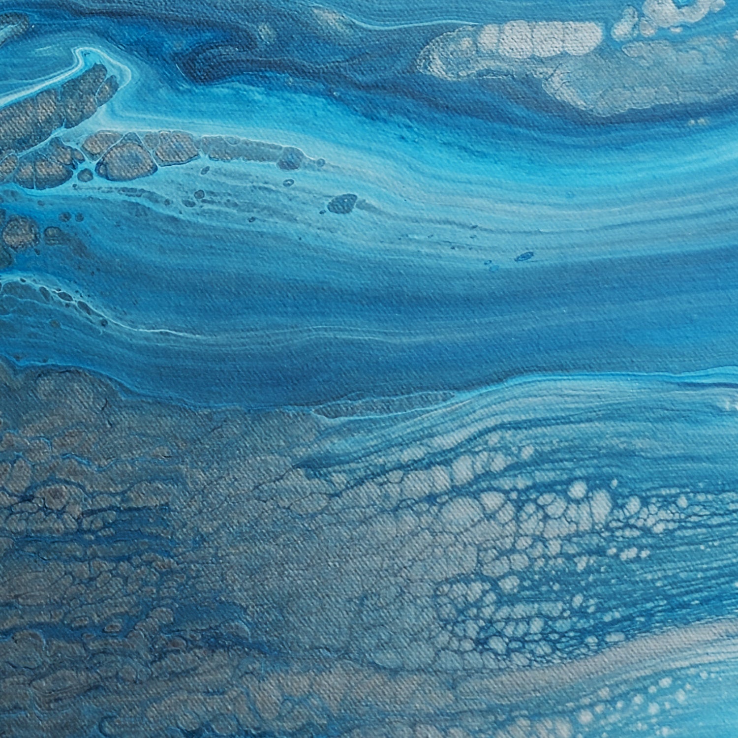 Close-up of square abstract acrylic painting in bright blue over stony pewter tones, clear shallow coastal water showing rock and sand below.